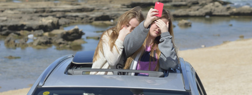 blonde teen girls with smart phone on the background of the sea in the car sunroof