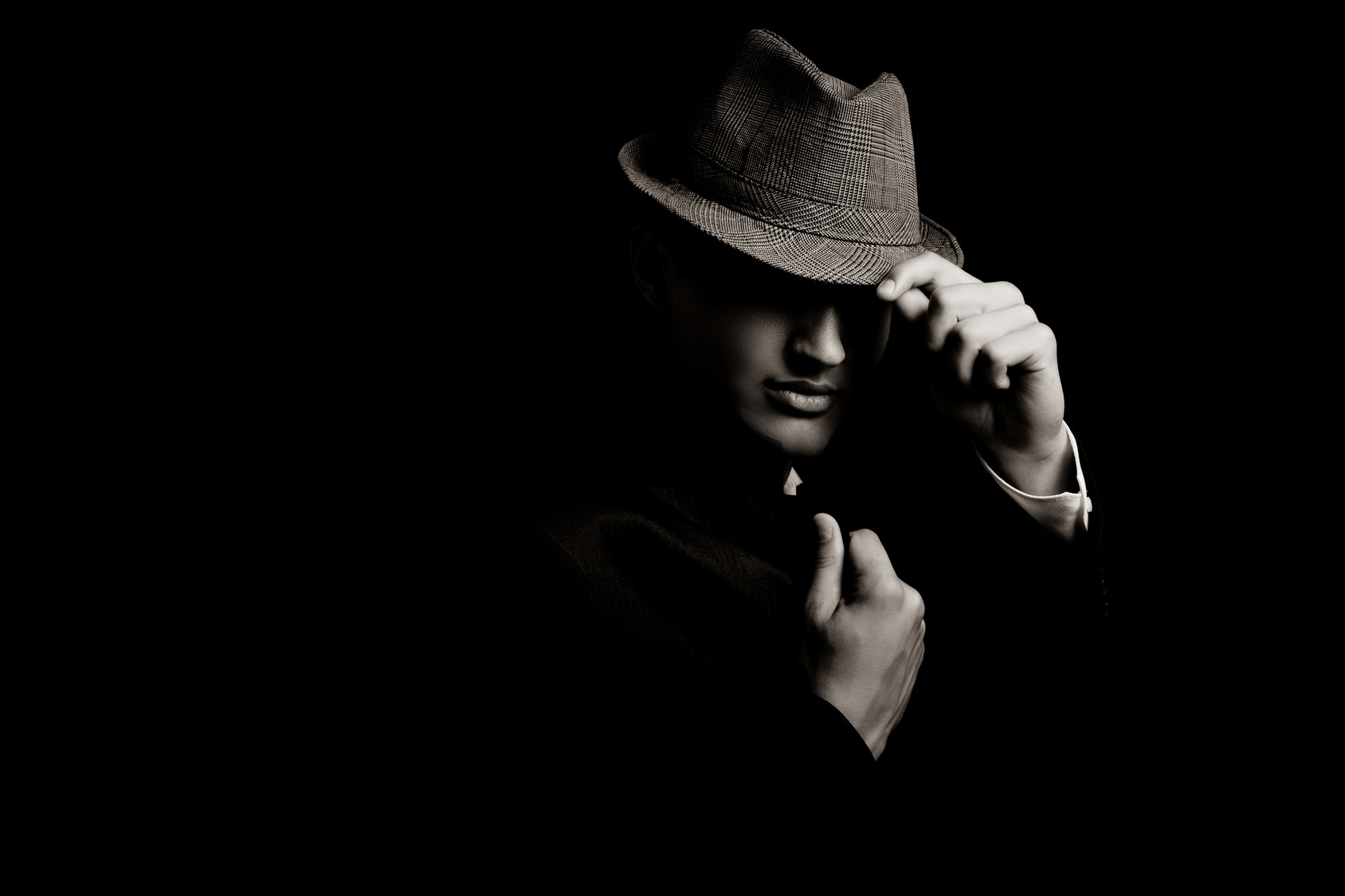 low key portrait of young gangster with hat in the darkness. Sepia toning.