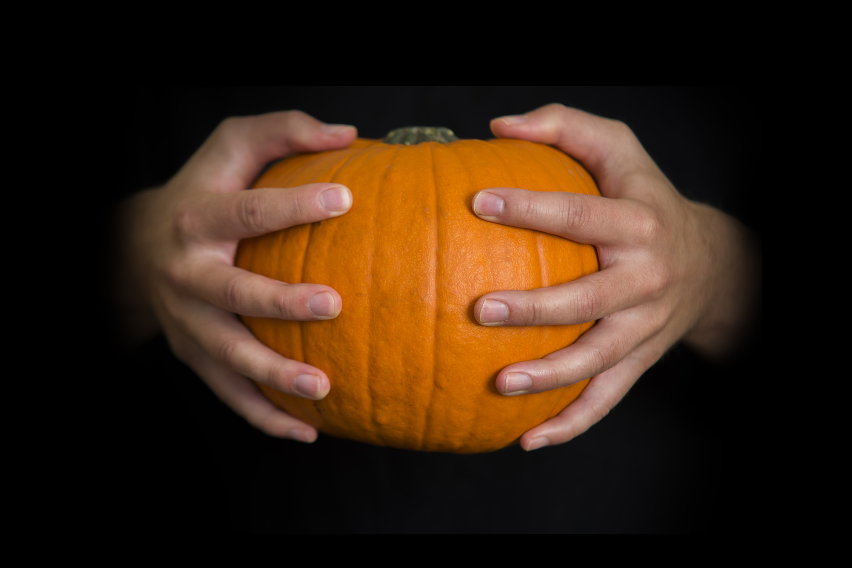 Hands holding a Halloween  pumpkin, with copy space on black