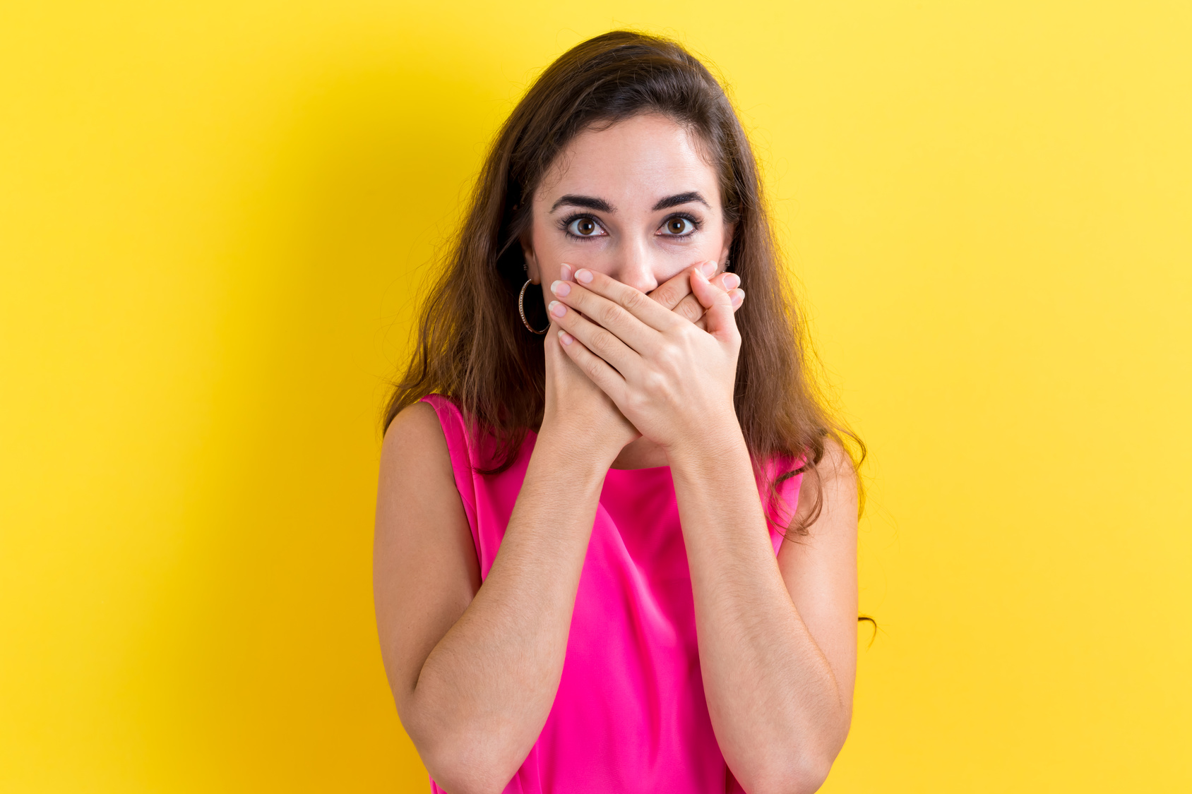 Young woman covering her mouth on a yellow background