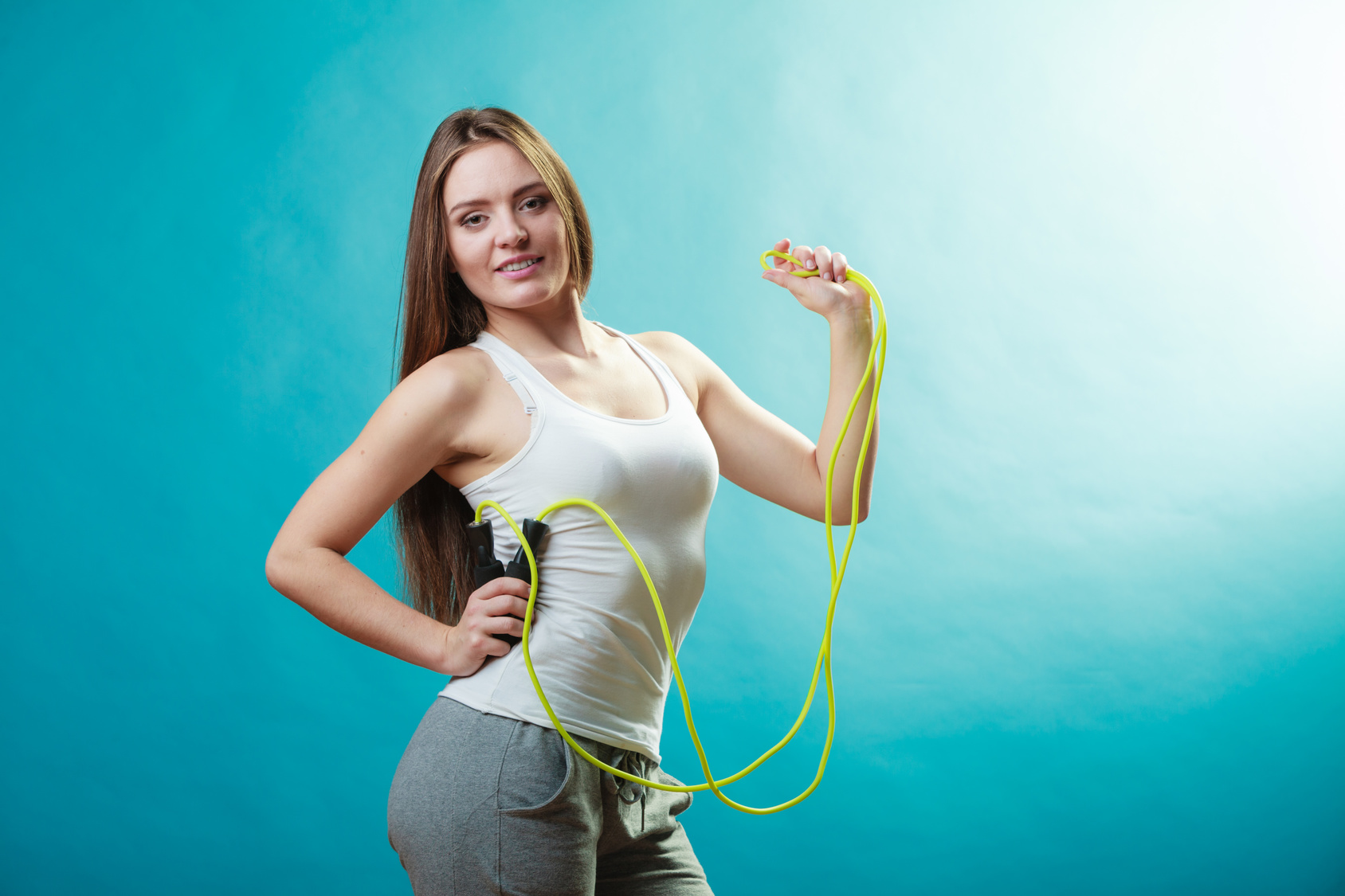 Young fit slim woman spend actively free time. Beauty happy girl wearing sports clothes with jumping skipping rope on blue background.