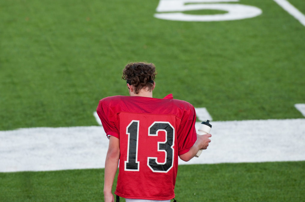 American football boy on sidelines during water during game.