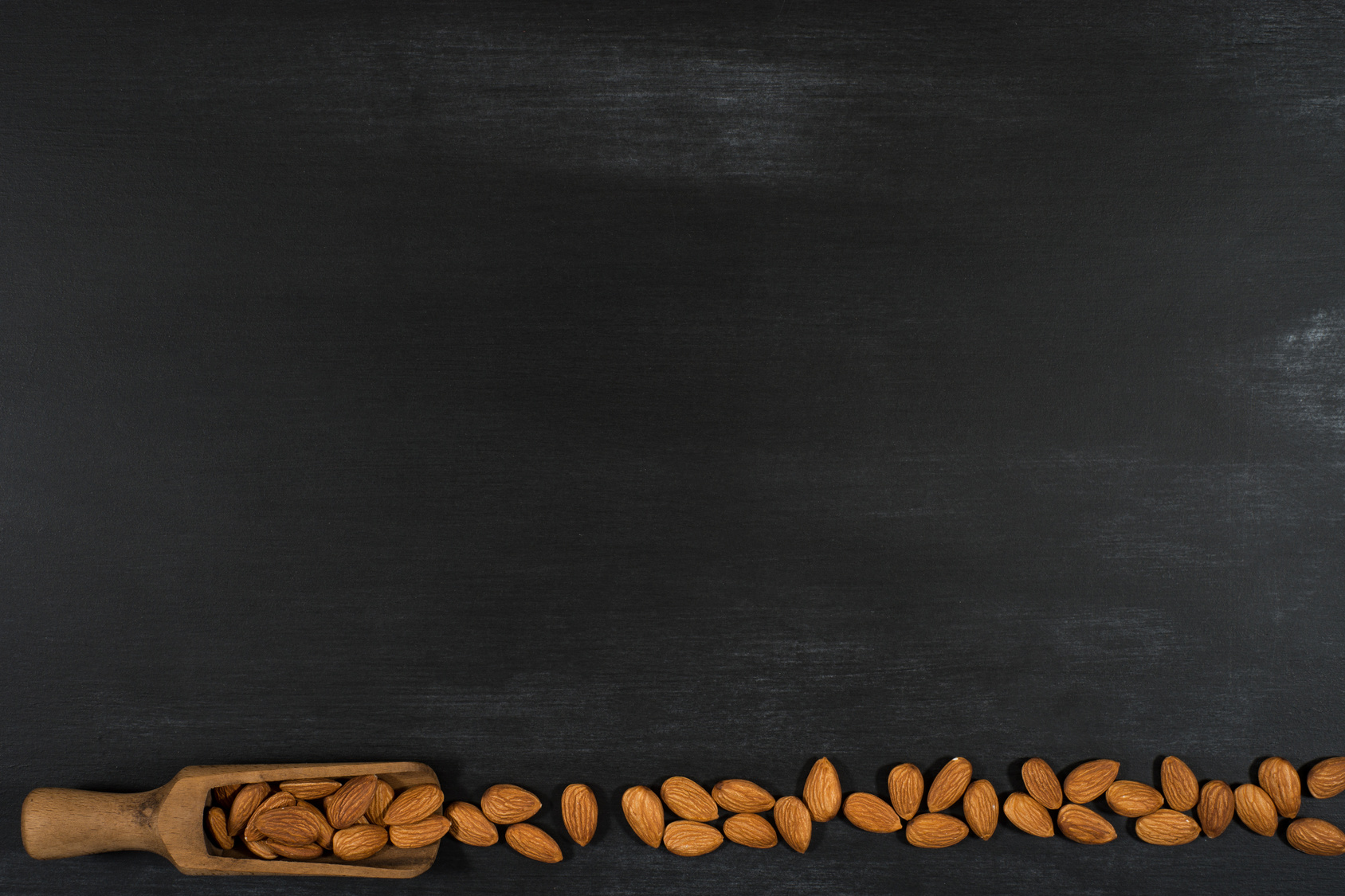 Almonds in a wooden scoop in a black chalkboard. Top view.