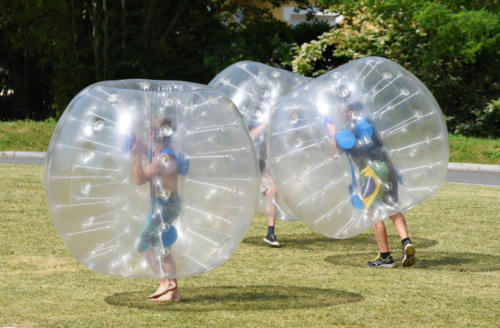 Several people are playing inside of the large transparent plastic spheres (orbs or zorbs) outdoors.