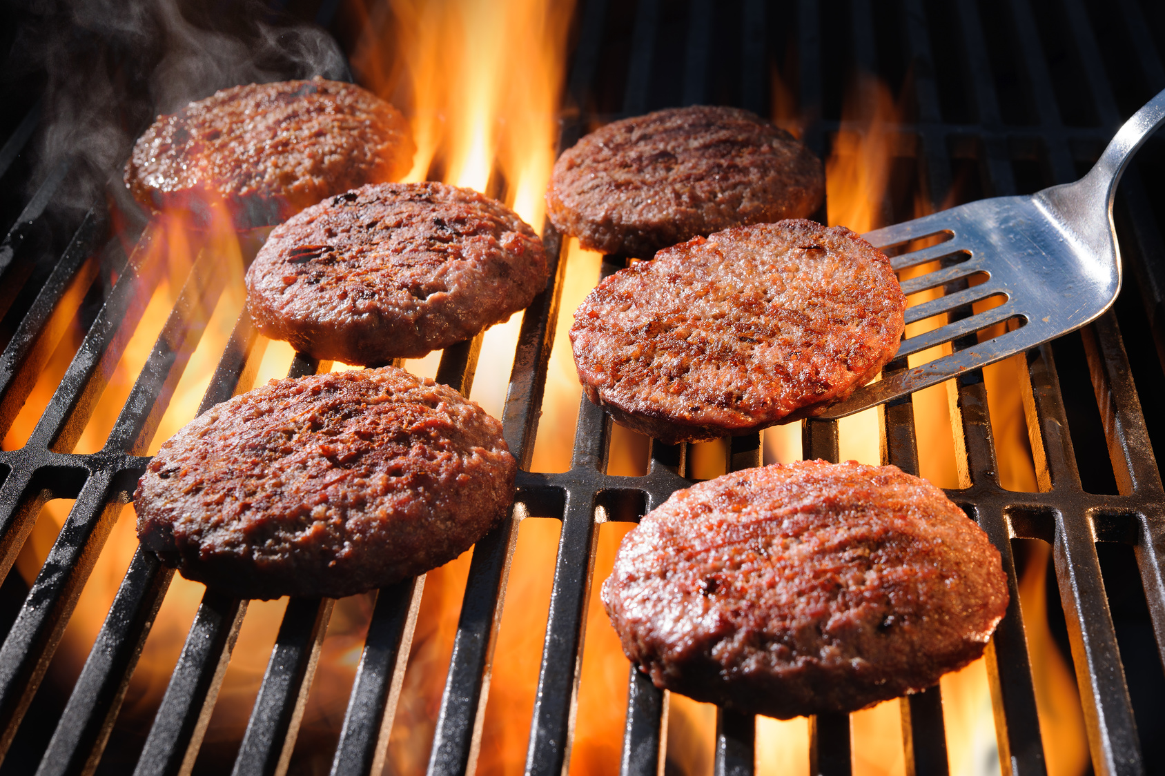 Juicy beef hamburger patties sizzling over hot flames on the barbecue